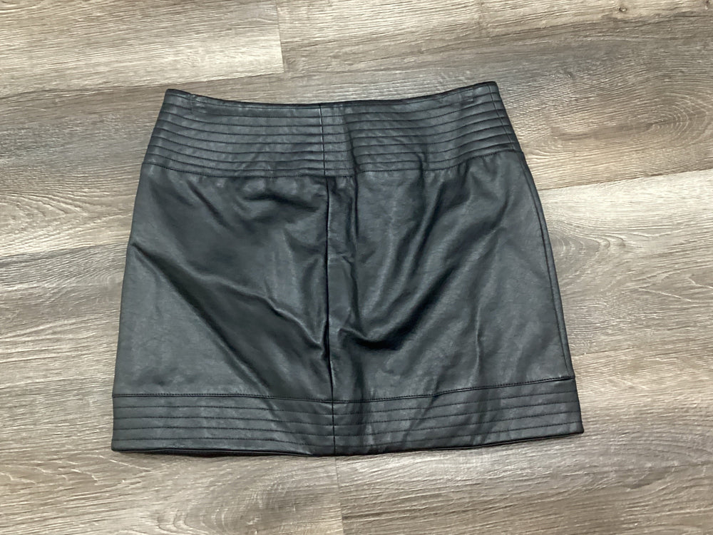 A black faux-leather mini skirt with horizontal stitched detailing at the waistband and hem, laid flat on a gray wood-look floor.